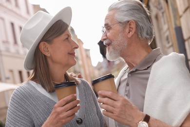Photo of Affectionate senior couple with coffee walking outdoors