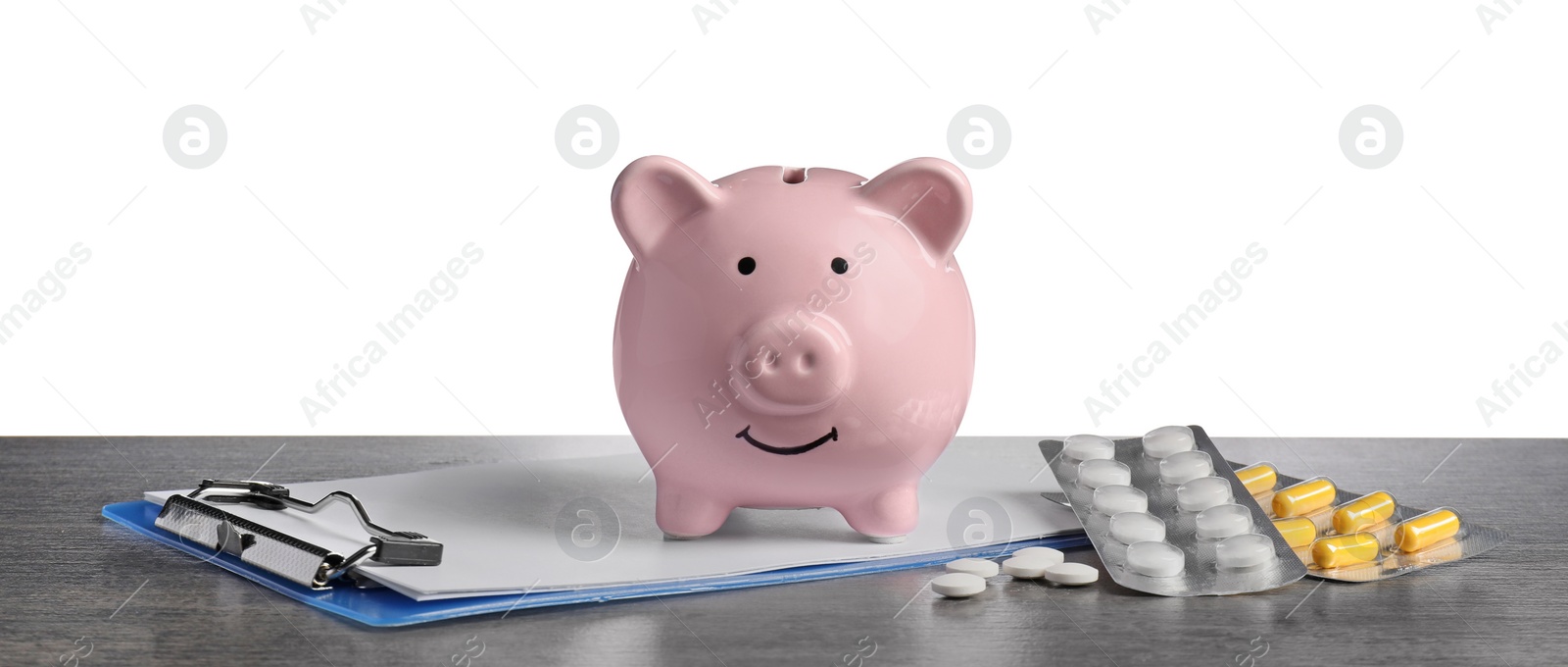 Photo of Piggy bank, clipboard and pills on dark grey table against white background. Medical insurance