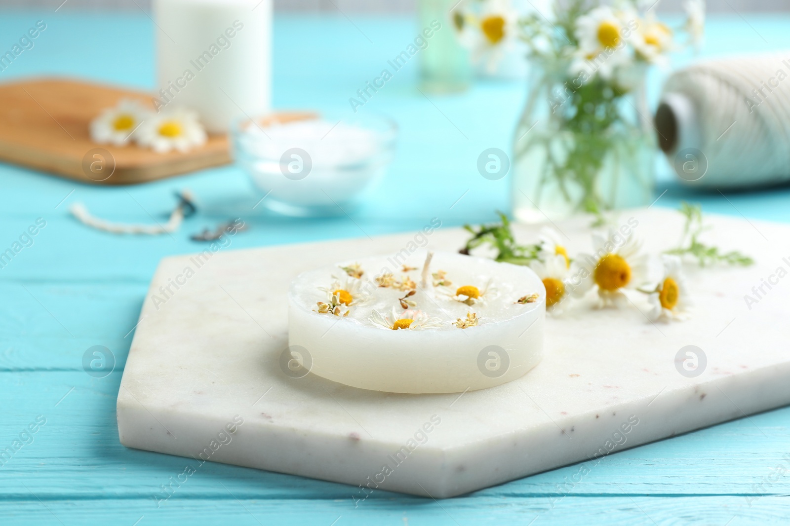 Photo of Board with floral candle and chamomile on color wooden table