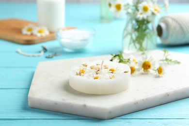 Photo of Board with floral candle and chamomile on color wooden table