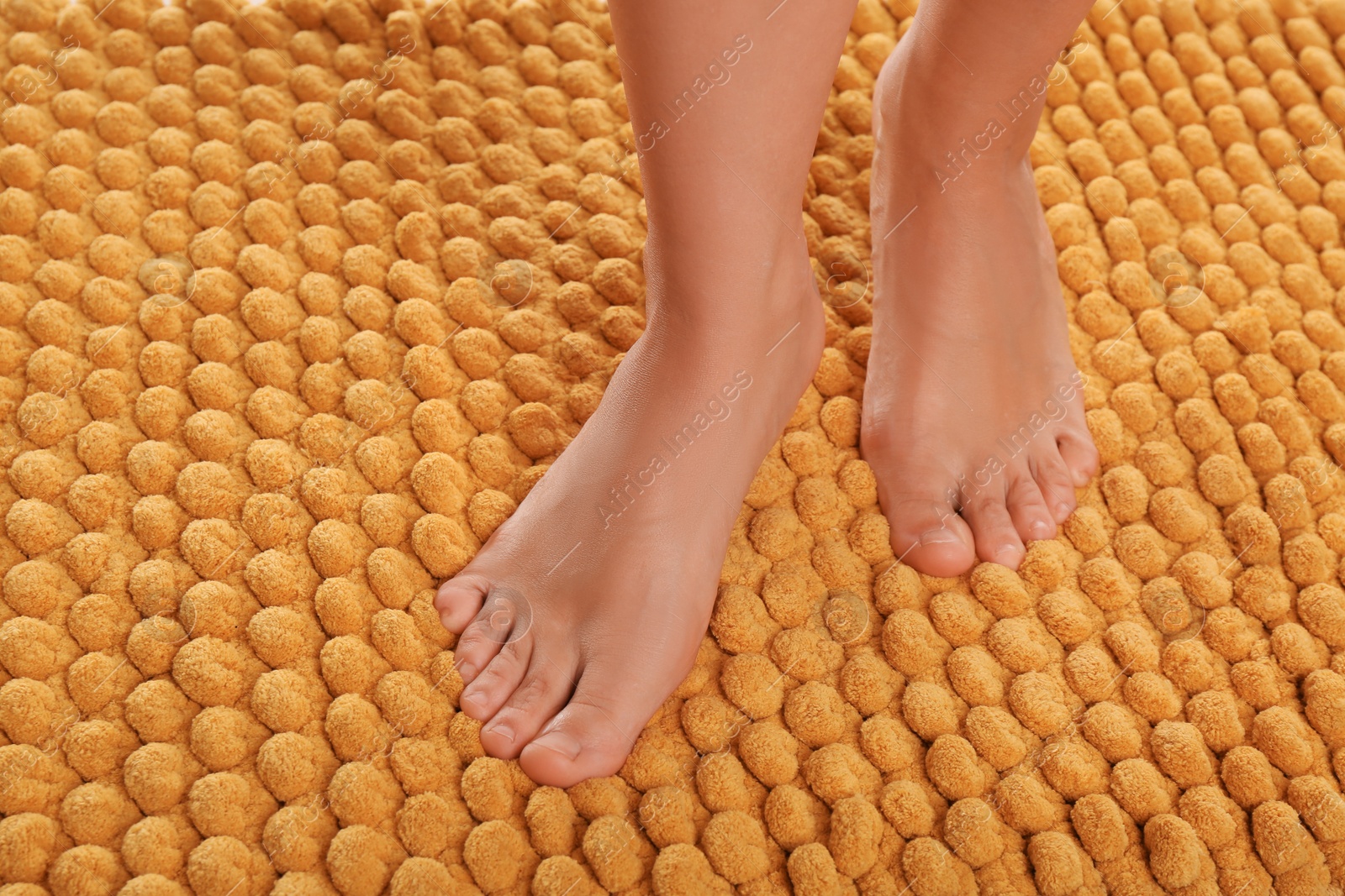 Photo of Woman standing on soft orange bath mat, closeup. Space for text