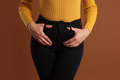 Photo of Woman wearing stylish black jeans on brown background, closeup