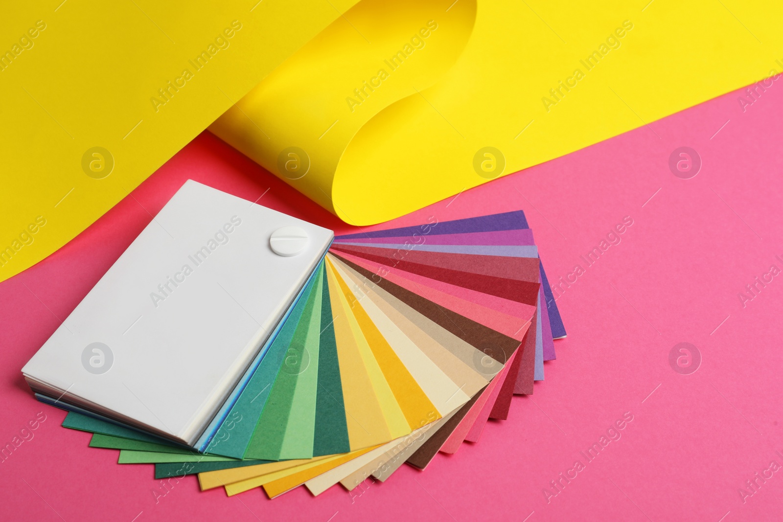 Photo of Color palette and yellow paper on pink background