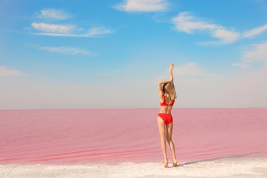 Photo of Beautiful woman in swimsuit posing near pink lake on sunny day