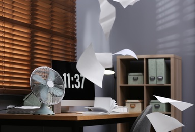 Photo of Modern electric fan and flying paper in office