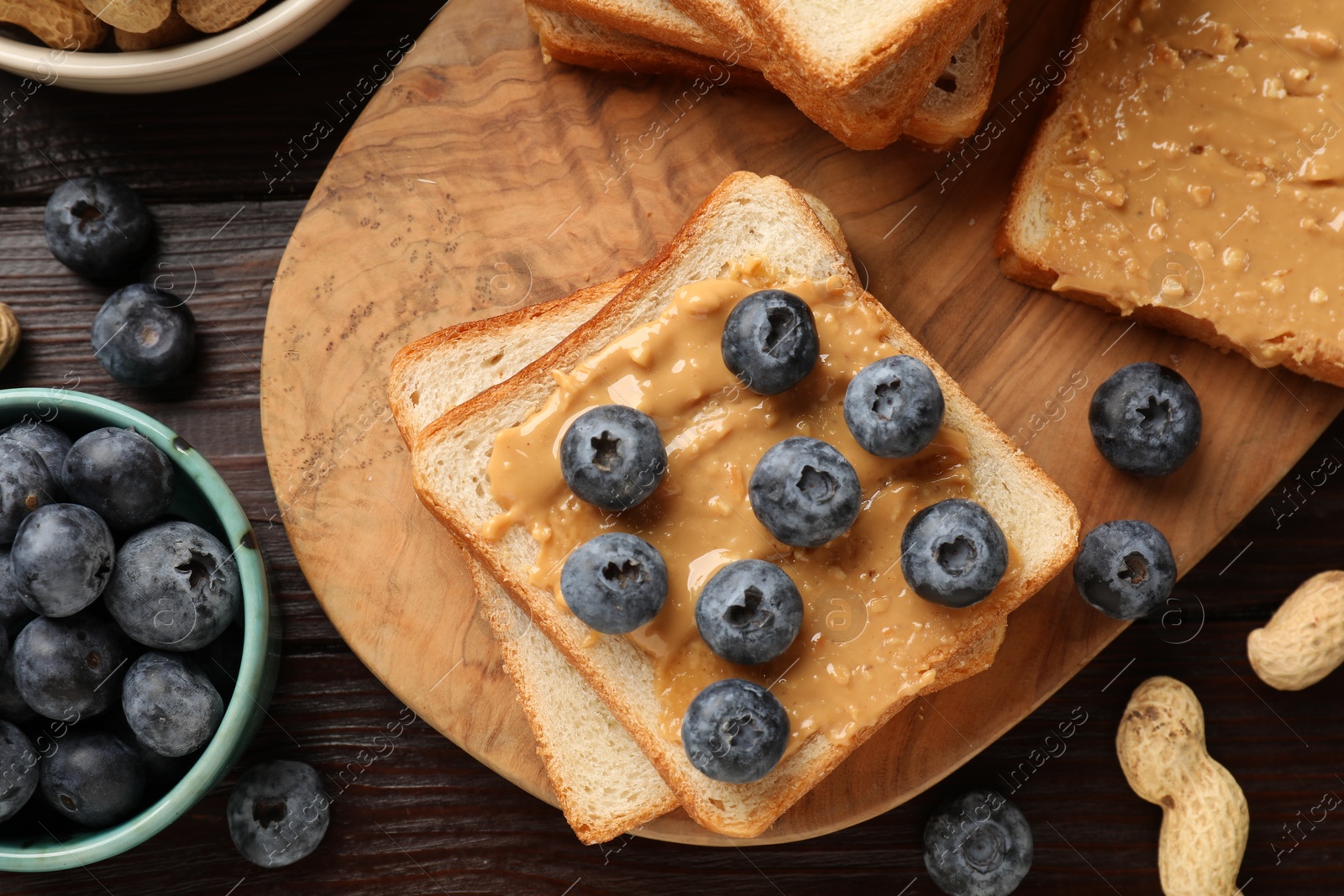 Photo of Delicious toasts with peanut butter, blueberries and nuts on wooden table, flat lay