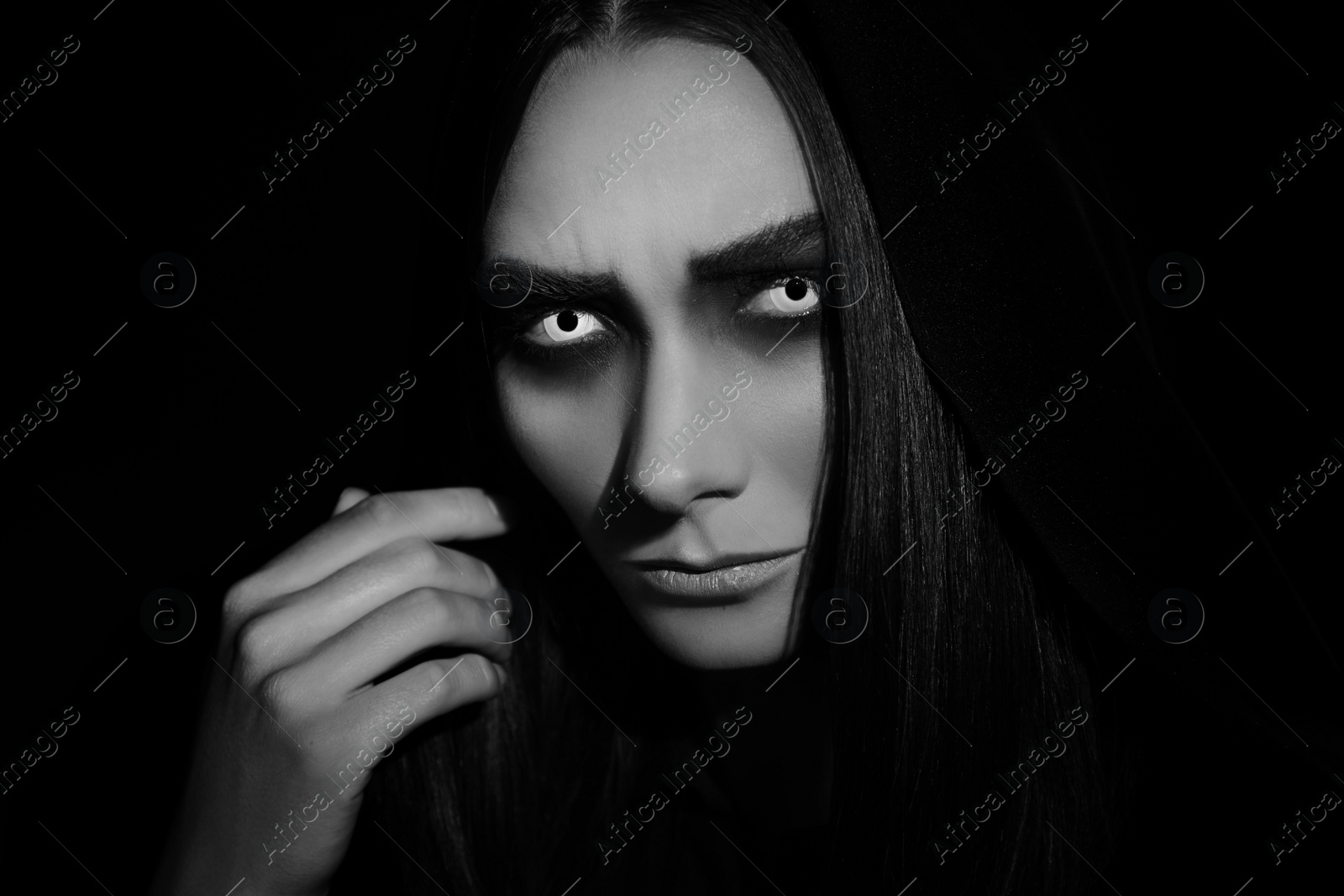 Photo of Mysterious witch with spooky eyes on dark background, closeup. Black and white effect