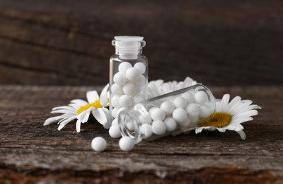 Photo of Bottles with homeopathic remedy and flowers on wooden table, closeup