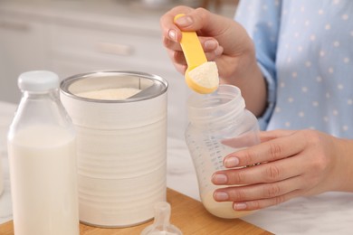 Photo of Woman preparing infant formula at table indoors, closeup. Baby milk