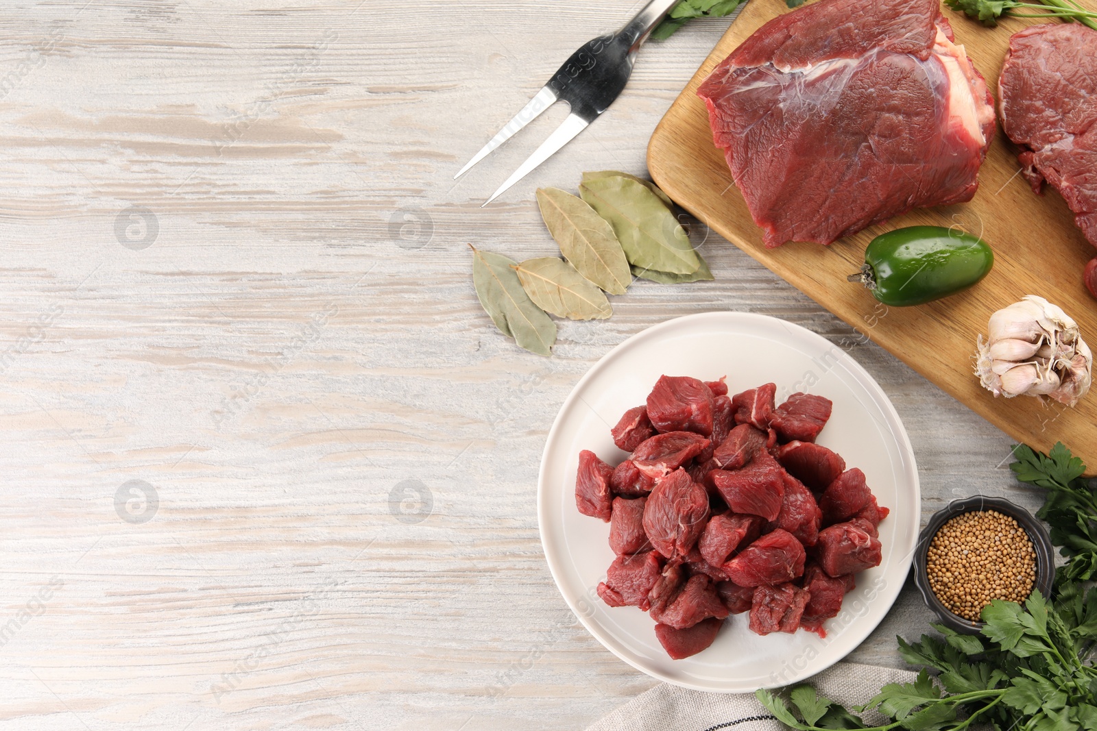 Photo of Pieces of raw beef meat, spices and products on light wooden table, flat lay. Space for text