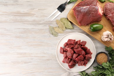 Photo of Pieces of raw beef meat, spices and products on light wooden table, flat lay. Space for text