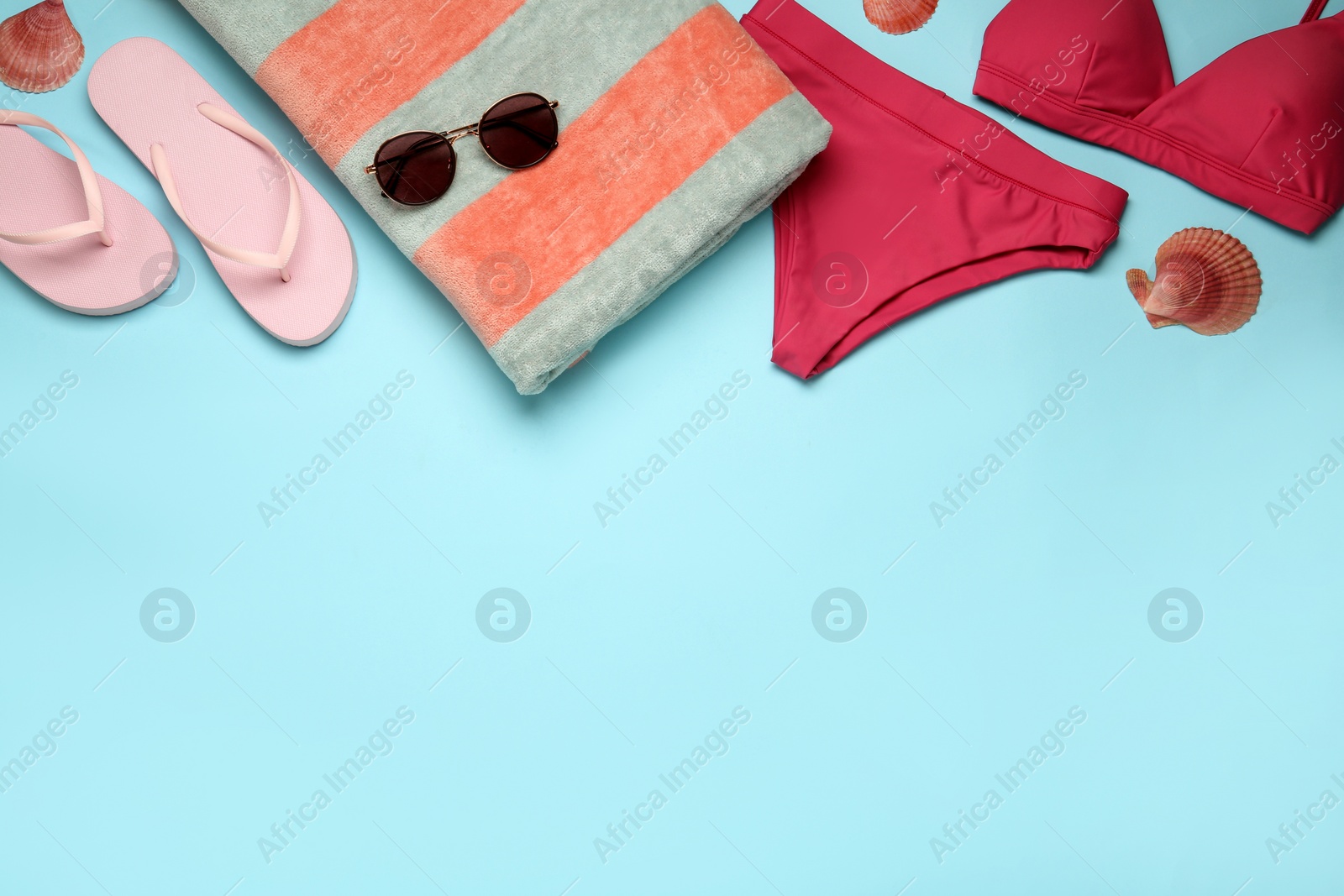 Photo of Beach towel, swimsuit, flip flops and sunglasses on light blue background, flat lay. Space for text