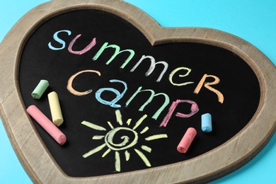 Heart shaped blackboard with text SUMMER CAMP, drawing and chalk sticks on color background