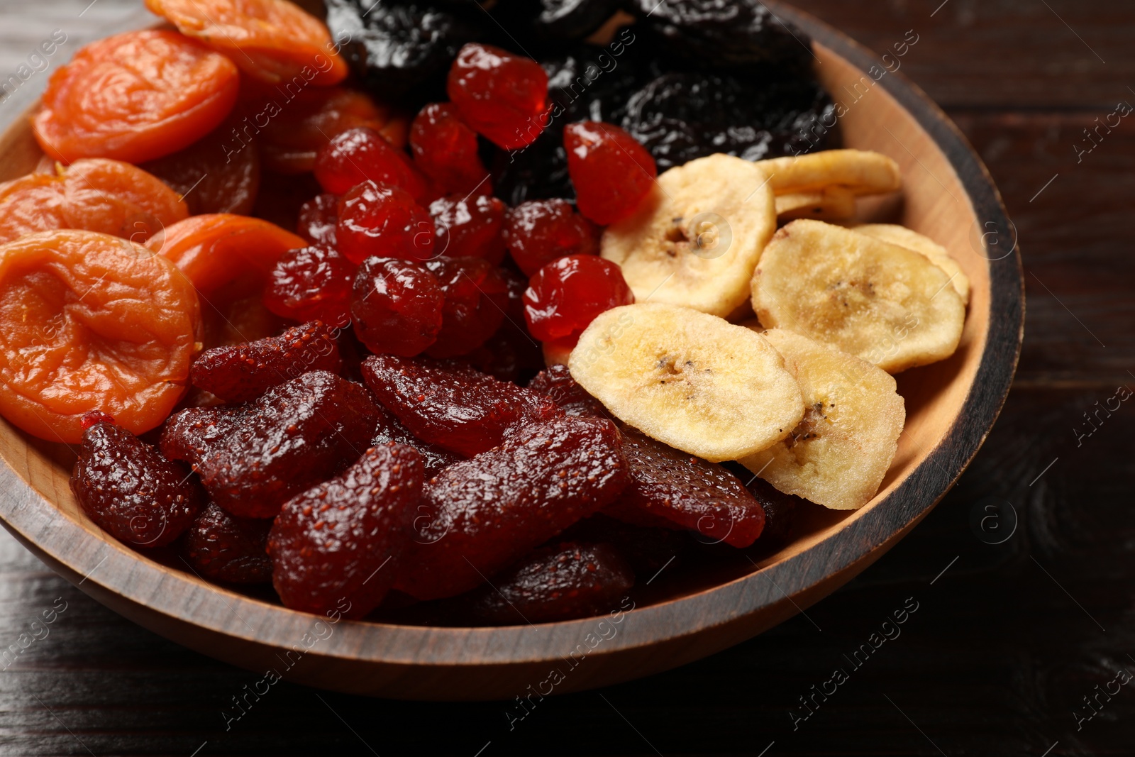 Photo of Mix of delicious dried fruits in bowl on wooden table, closeup