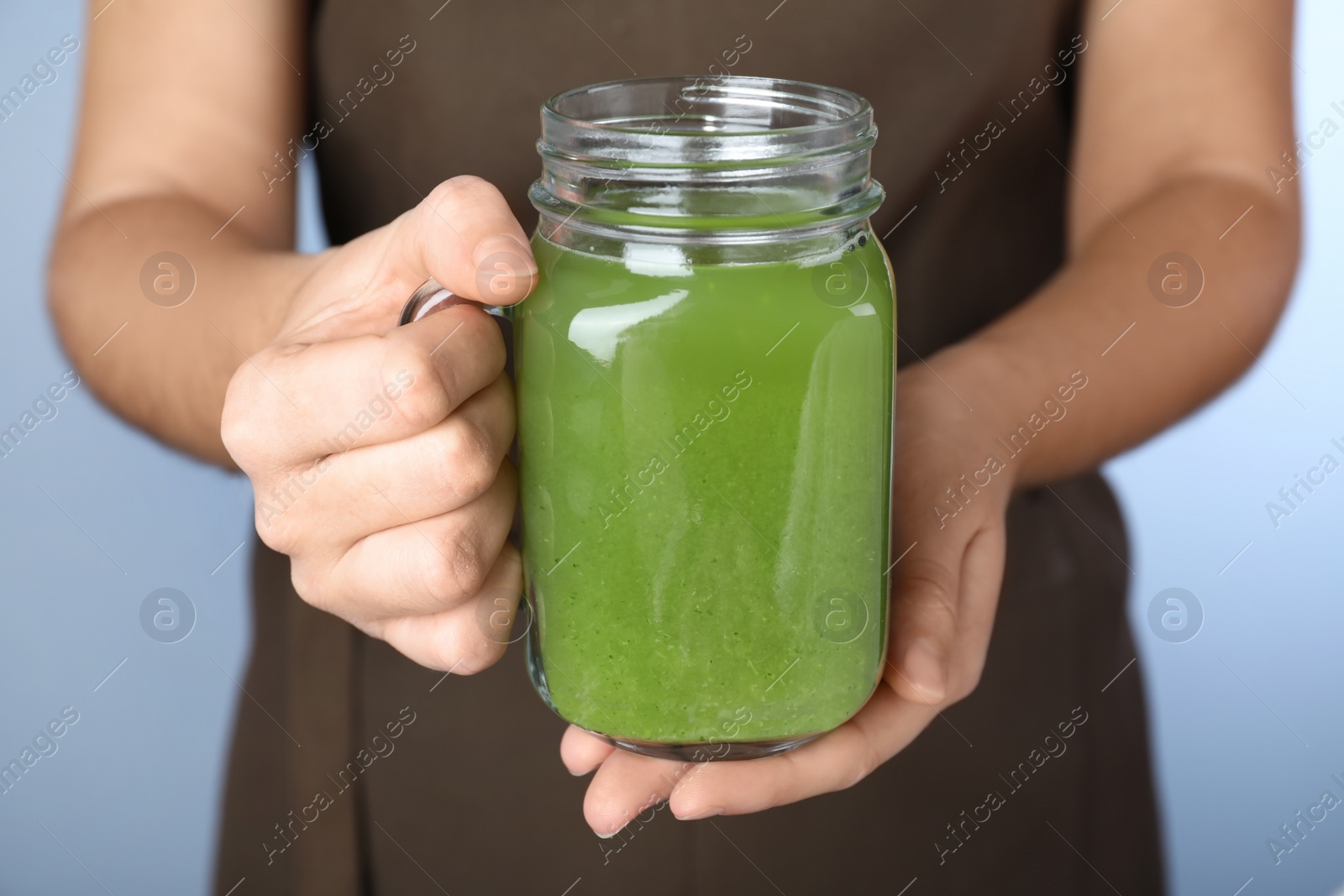 Photo of Woman holding mason jar with fresh celery juice on light blue background, closeup