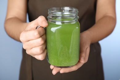 Woman holding mason jar with fresh celery juice on light blue background, closeup