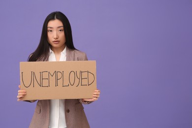 Photo of Asian woman holding sign with word Unemployed on purple background. Space for text
