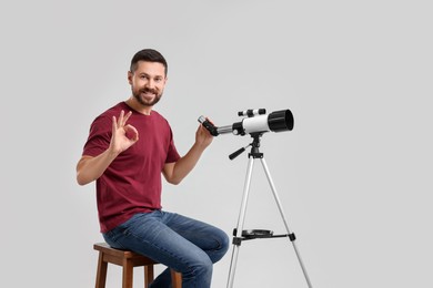 Photo of Smiling astronomer with telescope showing ok gesture on light grey background
