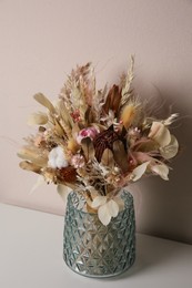 Photo of Beautiful dried flower bouquet in glass vase on white table near light grey wall
