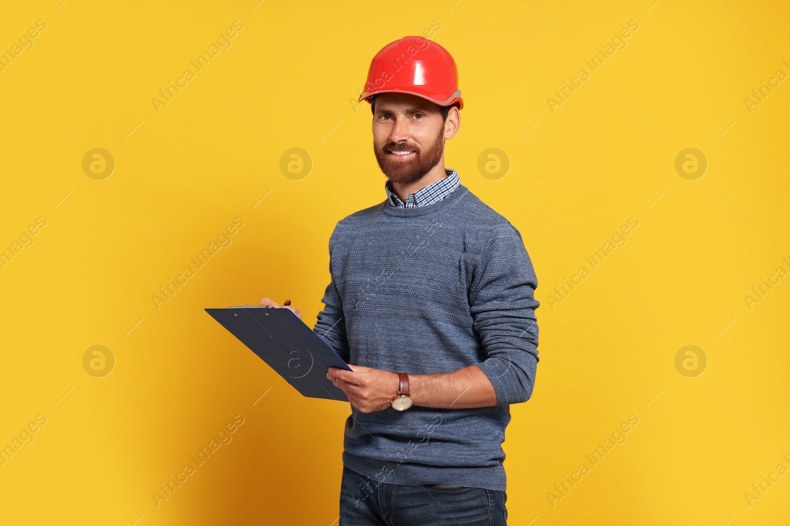 Photo of Professional engineer in hard hat with clipboard on yellow background