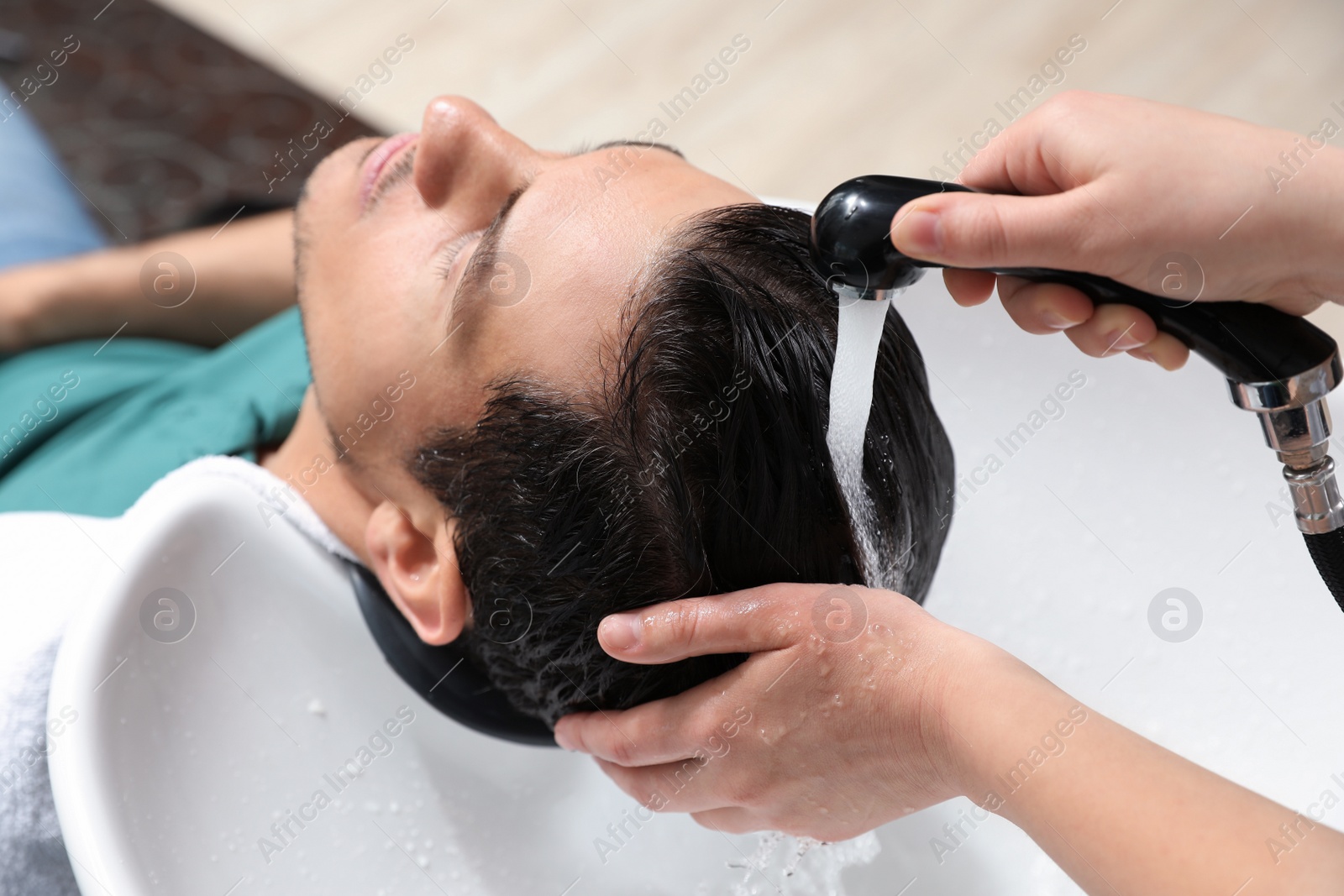 Photo of Stylist washing client's hair at sink in beauty salon