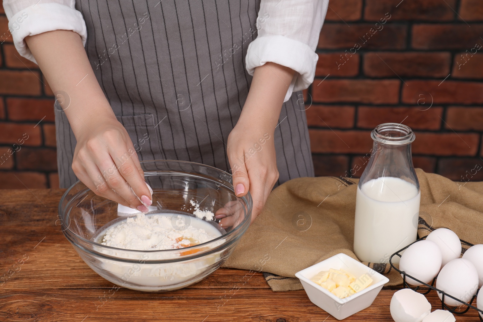 Photo of Preparing tasty baklava. Woman adding flour into bowl at wooden table, closeup