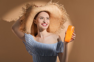 Beautiful young woman in sunlight holding sun protection cream on beige background
