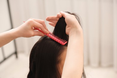 Hair styling. Professional hairdresser combing woman's hair indoors, closeup