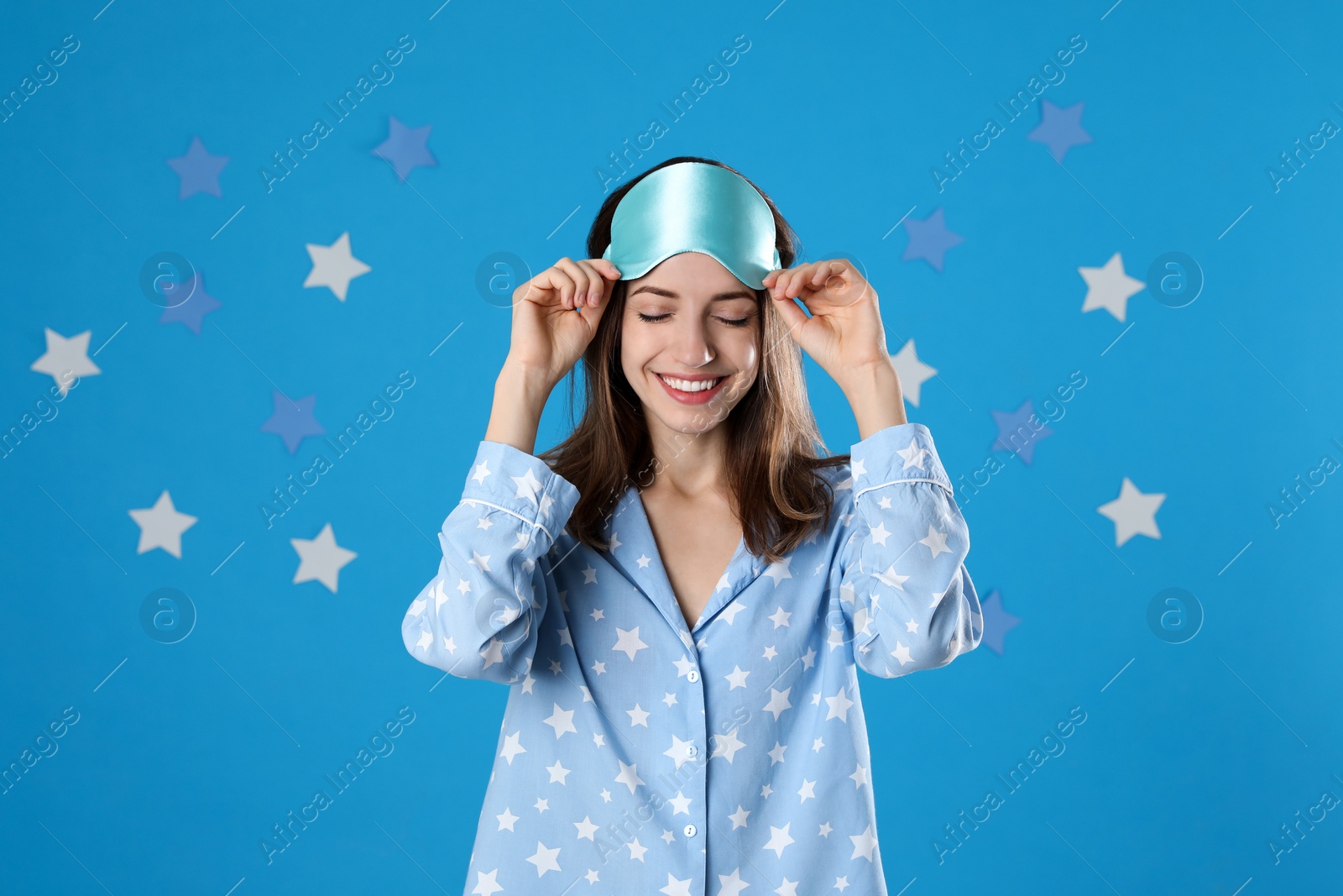 Photo of Beautiful woman wearing pajamas and sleep mask on light blue background. Bedtime