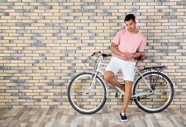 Photo of Handsome young hipster man with bicycle near brick wall