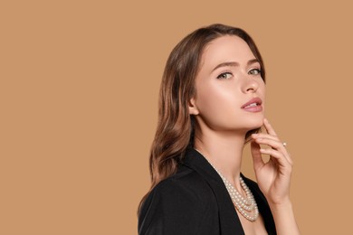 Photo of Young woman wearing elegant pearl jewelry on brown background, space for text