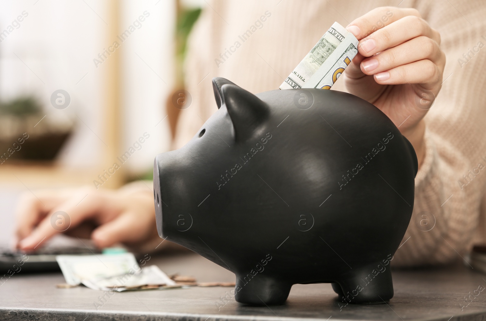Photo of Woman putting money into piggy bank at table indoors, closeup