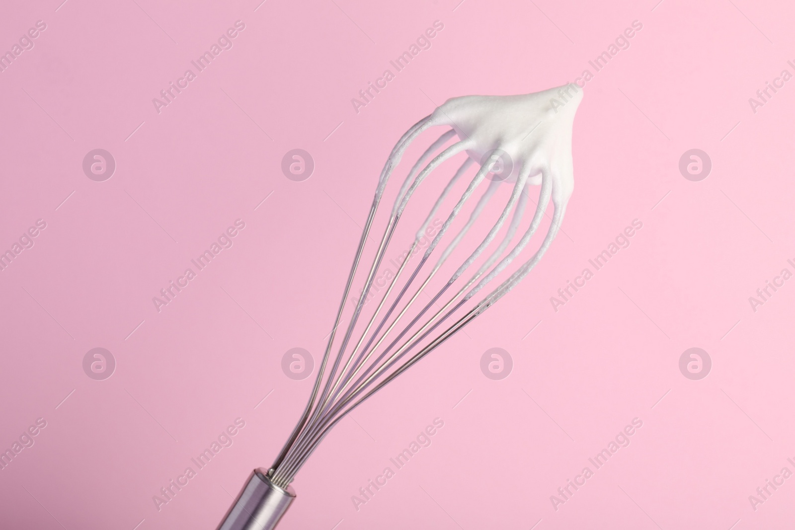 Photo of Whisk with whipped egg whites on pink background