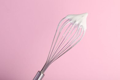 Photo of Whisk with whipped egg whites on pink background