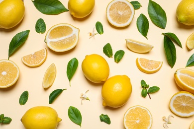 Many fresh ripe lemons with green leaves and flowers on beige background, flat lay