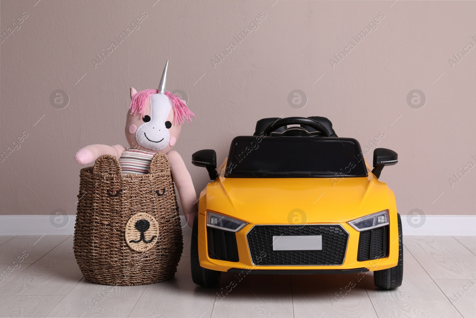 Photo of Child's electric car with toy unicorn in basket near beige wall indoors