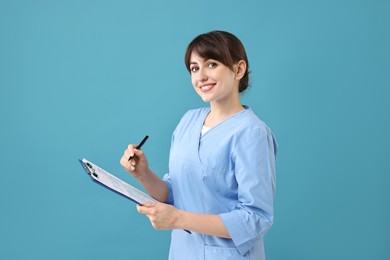 Photo of Portrait of smiling medical assistant with clipboard on light blue background