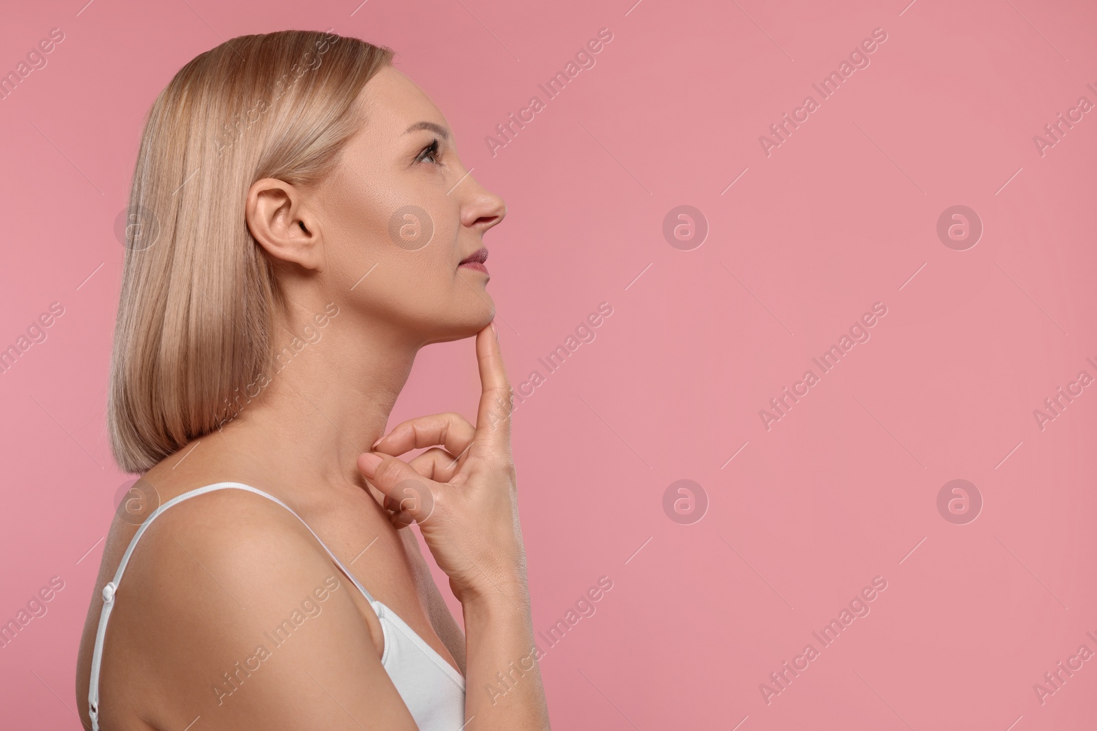 Photo of Beautiful woman touching her neck on pink background. Space for text