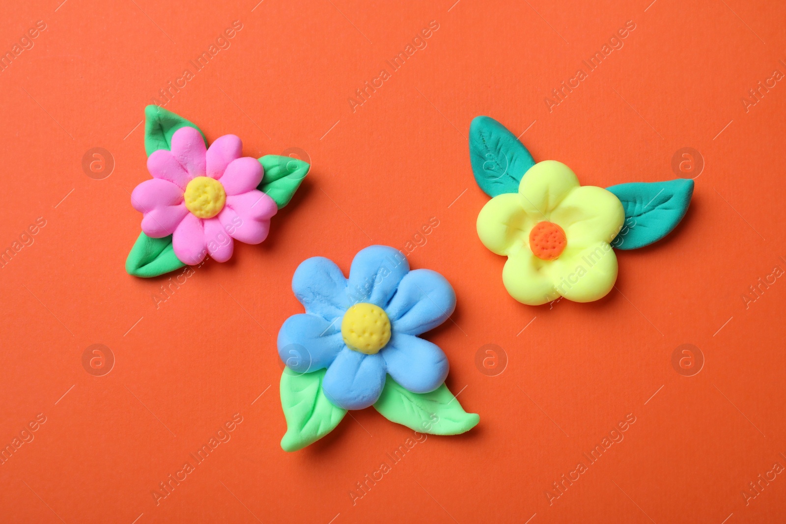 Photo of Colorful flowers with leaves made from play dough on orange background, flat lay