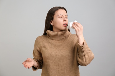 Photo of Young woman with tissue sneezing on light grey background. Runny nose