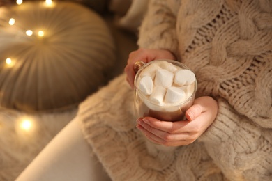 Photo of Woman holding cup of hot drink with marshmallow indoors, closeup