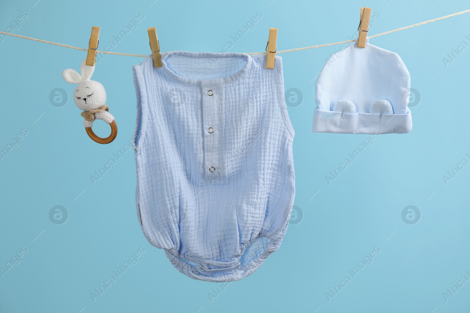 Photo of Baby clothes and accessories hanging on washing line against light blue background