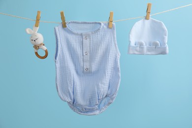 Baby clothes and accessories hanging on washing line against light blue background