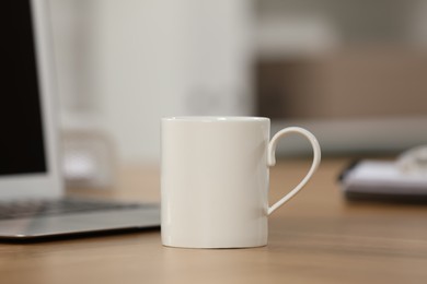 White ceramic mug and laptop on wooden table at workplace