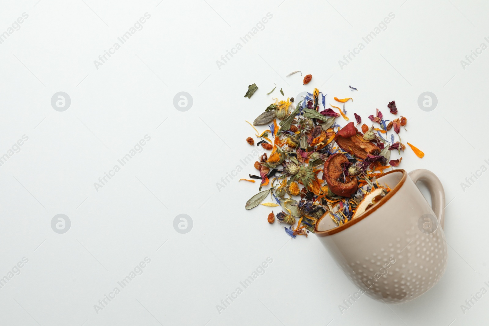 Photo of Overturned cup with dry herbal tea on white background, top view. Space for text