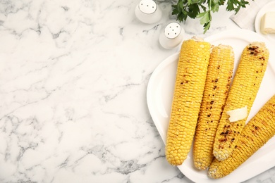 Photo of Fresh grilled corn cobs with butter on white marble table, flat lay. Space for text