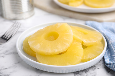 Photo of Tasty canned pineapple slices on white marble table, closeup