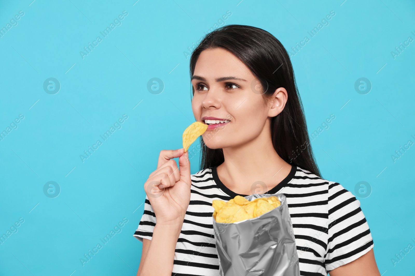 Photo of Beautiful woman eating potato chips on light blue background. Space for text