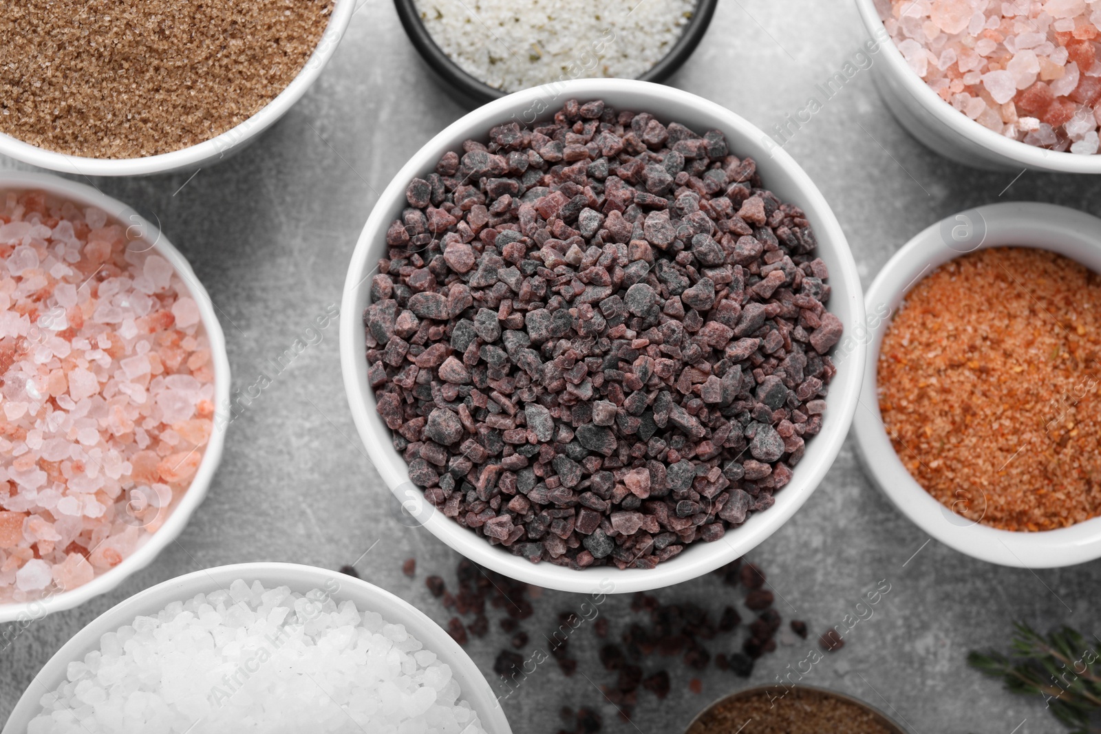 Photo of Different kinds of salt on grey table, flat lay