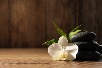 Photo of Spa stones, beautiful orchid flower and bamboo sprout on wooden table, space for text